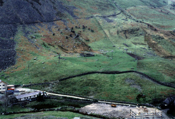 This view, which looks north-west, shows some of the extensive industrial remains on the valley floor in the foreground, while the scheduled hut group settlement is located on the level area at the foot of the mountain which shows as a green patch in the centre of the photograph.