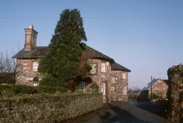 The public house (Ty'n Llan or The Harp) in the centre of the village, with the churchyard wall to the right and the end of one of the terraces of houses just visible in the background.